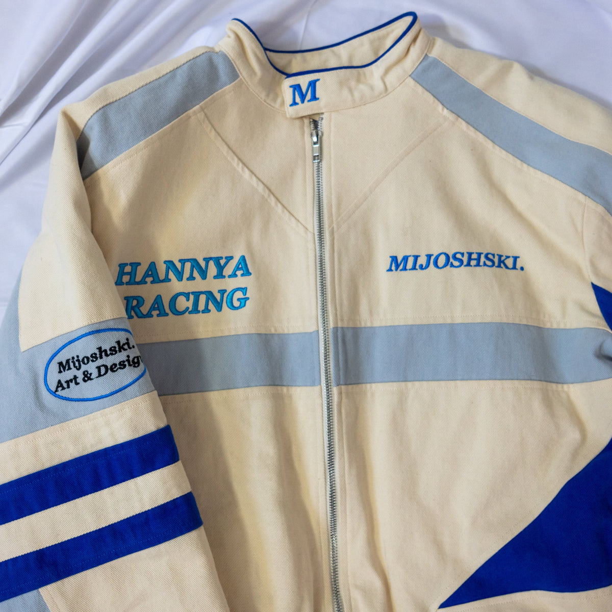 Beige racing jacket with blue and gray accents on a white background