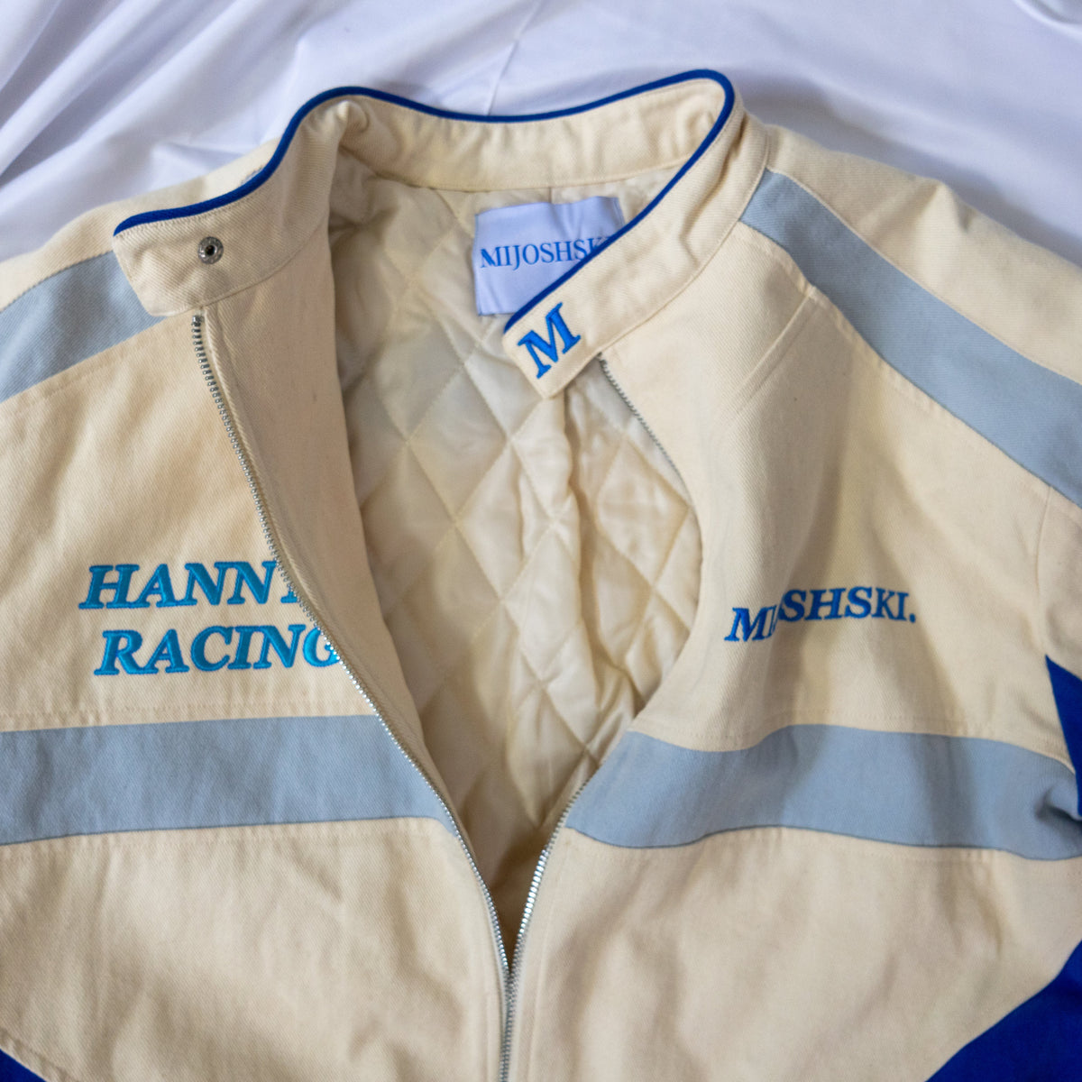 Beige racing jacket with blue and gray accents, featuring 'Hannya Racing' and 'Mijoshski' branding.
